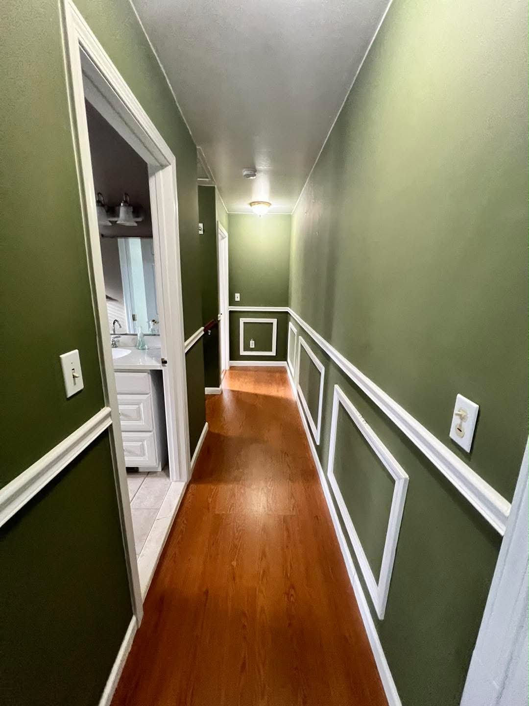 Hunter green hallway with white wainscoting and picture-frame wall trim