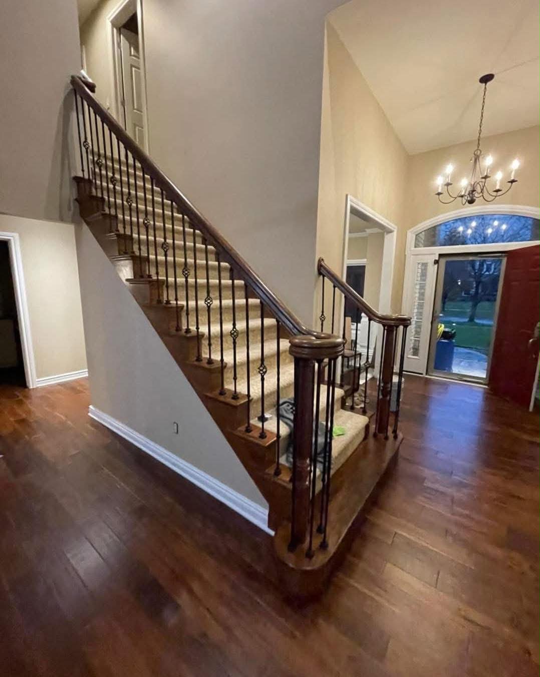 Grand entry staircase with dark wood rail, wrought iron balusters, and hardwood floors